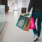 person walking while carrying a camera and paper bags